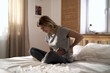 © gpointstudio - Close up of woman with pain of belly and back sitting on the bed at home