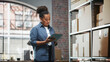 © Gorodenkoff - Inventory Manager Checks Stock, Writing in Clipboard Software on Tablet Computer. Black Woman Working in a Warehouse Storeroom with Rows of Shelves Full of Parcels, Packages Ready for Shipment.