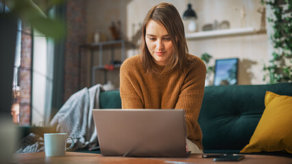 Poster - Portrait of Smiling Young Woman Working from Home on Laptop Computer in Sunny Cozy Apartment. Successful Creative Girl Entrepreneur Does Remote for e-Business Project, Online Shopping