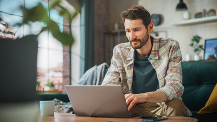 Poster - Portrait of Smiling Middle Aged Man Working from Home on a Laptop Computer in Sunny Cozy Apartment. Successful Male Entrepreneur Does Remote for e-Business Project, Online Shopping