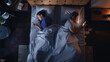 Top View Apartment Bedroom: Young Couple Lying in Bed, Both Using Smartphones. Family of Two Using Mobile Phones to Browse Social Media, Communicate, Search internet, do Online Shopping Before Sleep