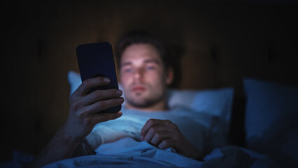 Leinwandbilder - Caucasian Man Uses Smartphone in Bed at Home at Night. Handsome Guy Browsing Social Media, Reading News, Doing Online Shopping, Chatting with Friends Late at Night.
