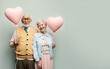 © Uncanny Valley - A married couple of pensioners who are happy in love and have a matching outfit of pastel colors. Love that lasts forever. Grandparents holding a heart shaped balloon. Illustration. Generative AI.