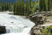 Female Hiker Standing On Top Of Rock Cliff Overlooking Waterfalls And Rushing River, West Of Turner Valley; Alberta, Canada