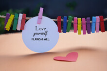 Self Love And Care Concept. Inspirational Motivational Quote - Love Yourself Flaws And All. With Text Message On White Circle Paper, Red Heart And Colorful Wooden Clips. Self Love And Care Concept.