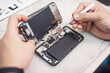 © guruXOX - Cell phone repair at service center, smartphone disassembling and diagnostics, repairman workplace top view