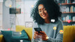 Social Media Visualization Concept: Happy Black Woman Uses Smartphone at Home. 3D Representation of Social Media Posts, Smiley Faces, e-Commerce Online Shopping Digital Icons Flying Around the Device