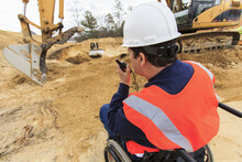 Construction engineer with spinal cord injury talking on portable radio with equipment operators