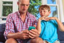 Father And Son With Hearing Impairments Signing 'email' On Cellphone In American Sign Language On Couch