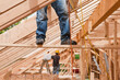 © Designpics - Hispanic carpenters pulling up air hose while standing on support board at a house under construction