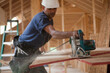 © Designpics - Hispanic carpenter trimming roof panel with a circular saw at a house under construction