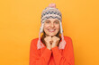 © sementsova321 - Portrait of cute delighted Caucasian woman wearing funny earflap hat and orange casual jumper, looking at camera, keeps fists under chin, standing isolated over yellow background.