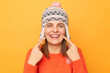 © sementsova321 - Horizontal shot of delighted young adult woman wearing funny earflap hat and orange casual jumper standing isolated over yellow background, pointing at her teeth after visiting dentist.