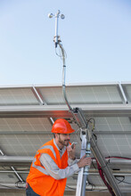 Power engineer on a cell phone while holding weather station conduit at solar photovoltaic array