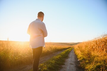 Farmer walking in corn fields with beautiful sunset