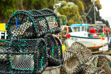 Close-up Of Lobster And Crab Cages Stacked Up, With Fishing Boat In The Background; Cornwall County, England