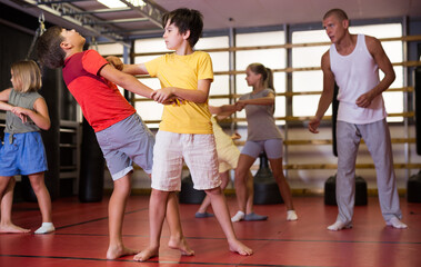 Wall Mural - Girls and boys performing self-defence moves in gym during their group training.