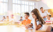 © JackF - Girl and boy sitting at desk in classroom with their classmates, listening to teacher explaining lesson subject.