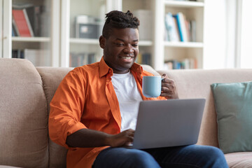 Wall Mural - Relaxed black guy watching movie and drinking tea at home