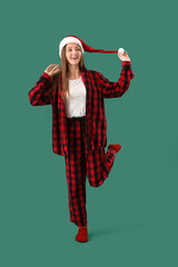 Sticker - Young woman in Santa hat and checkered pajamas on green background