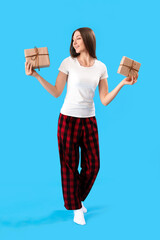 Poster - Young woman in pajamas with Christmas gifts on blue background