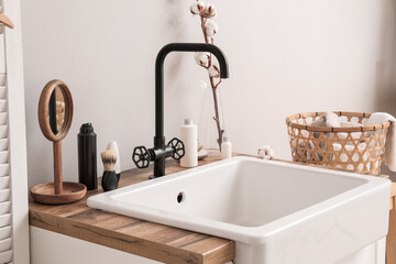 Table with ceramic sink, bath accessories and cotton flowers near light wall