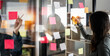 Team or staff discussing with sticky notes a schedule on glass wall for future project together, innovation and vision business meeting in a modern office,  working on a business marketing strategy.