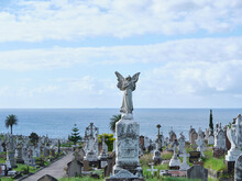 Sculpture Of An Angel In The Cemetery With Cross Sculptures And Grave Stones And A View Of The Ocean