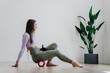 Wonderful brunette girl in sportswear with artificial hand stretching at home using massage roll with big plant on background. Rehabilitation after injury. Equality for people after orthopaedics.