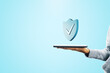 © Who is Danny - Close up of female hand holding tablet with creative antivirus shield icon on light blue background with mock up place. Secure phone usage, protection and web safety concept.