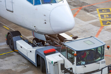 Airplane execute push back operation at airport, close up view. Tug tractor truck new type elevator chassis.