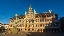 View Of Brabo Fountain In Front Of Antwerp City Hall Richly Ornamented With Heraldic Symbols, Sculptures And Flags Belgium, Flanders And Countries Of European Union And United Nations On Grote Markt..