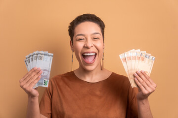 cheerful afro brazilian woman celebrating successful business money in all beige colors. financial, profit, credit, purchase, rich concept. 