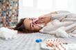© _KUBE_ - A young Caucasian woman is lying on the bed next to medicines, blowing her nose in a handkerchief. Side view. Concept of viral infection and quarantine