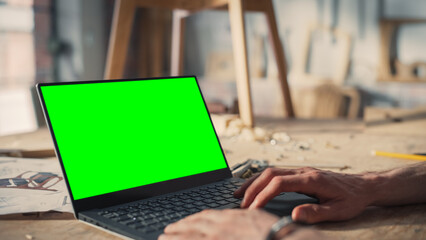 Close Up Shot of a Person Using Laptop Computer with Green Screen Chroma Key Display. Creative Man Working in Carpentry Studio Workshop.