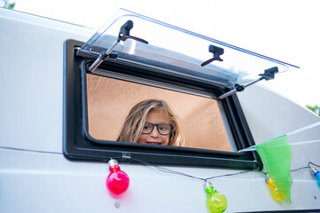 Happy boy sticks his head out of the van window on a wonderful day at camp. Van life concept.