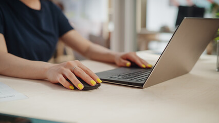 Poster - Female Employee in Black Casual Clothes Working on Laptop in Office During a Sunny Day. Close Up on Hands with Striking Yellow Nail Polish Typing Texts on a Computer, Writing Emails and Using Mouse.