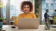 © Gorodenkoff - Portrait of a Beautiful Middle Eastern Manager Sitting at a Desk in Creative Office. Young Stylish Female with Curly Hair Looking at Camera with Big Smile. Colleagues Working in the Background.