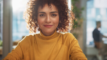Aufkleber - Portrait of a Beautiful Middle Eastern Manager Sitting at a Desk in Creative Office. Young Stylish Female with Curly Hair Looking at Camera with Big Smile. Colleagues Working in the Background.