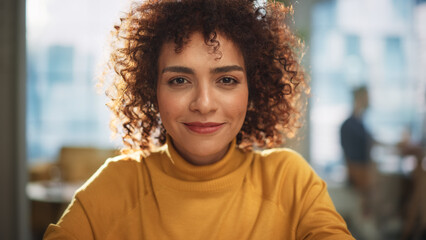 Wall Mural - Portrait of an Attractive Arab Female Sitting at a Desk in Creative Agency. Young Stylish Manager with Curly Hair Smiling, Looking at Camera. Manager Working in Modern Company.