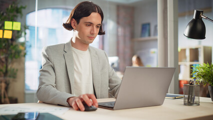 Fototapete - Creative Project Manager Sitting at a Desk, Working on a Laptop Computer in an Office. Handsome Marketing Specialist in a Casual Jacket Planning a Project, Browsing Internet and Writing Emails.