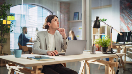 Aufkleber - Handsome Long-Haired Employee Sitting at a Desk in Creative Agency. Stylish Man Using Laptop Computer in Marketing Company. Colleagues Working in the Background. Rack Focus Portrait.