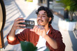© Austockphoto - Smiling curly haired man taking a picture using his mobile phone on the sidewalk