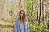 Fototapeta Las - Portrait of a model girl in a gray coat. A beautiful girl with long hair and a gray coat in the forest among the trees.