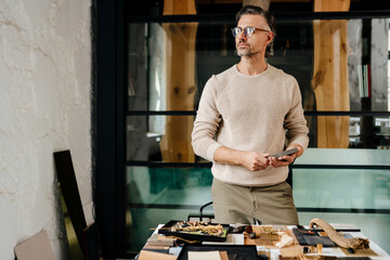 Sticker - Mature man in eyeglasses examining samples while working at office