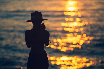 Wall Mural - Silhouette woman standing in ocean sea during summer sunset on blurred background.