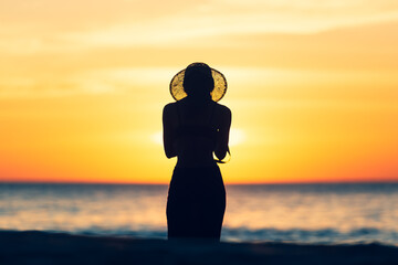 Wall Mural - Silhouette woman standing in ocean sea during summer sunset on blurred background.