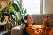 © Drobot Dean - Young white woman in headphones using cellphone while lying on couch