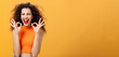 Charismatic happy and joyful attractive young female with curly hairstyle showing okay gestures with both hands in approval or confirmation smiling and laughing happily over orange wall