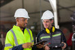 Two male engineer workers discuss and holding digital tablet working in the industry factory